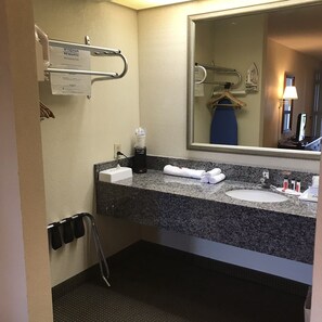 A hotel bathroom with a granite countertop, a sink, a mirror, a towel rack, and a hand dryer.