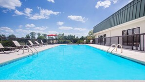 Una piscina con lettini e un ombrellone rosso.