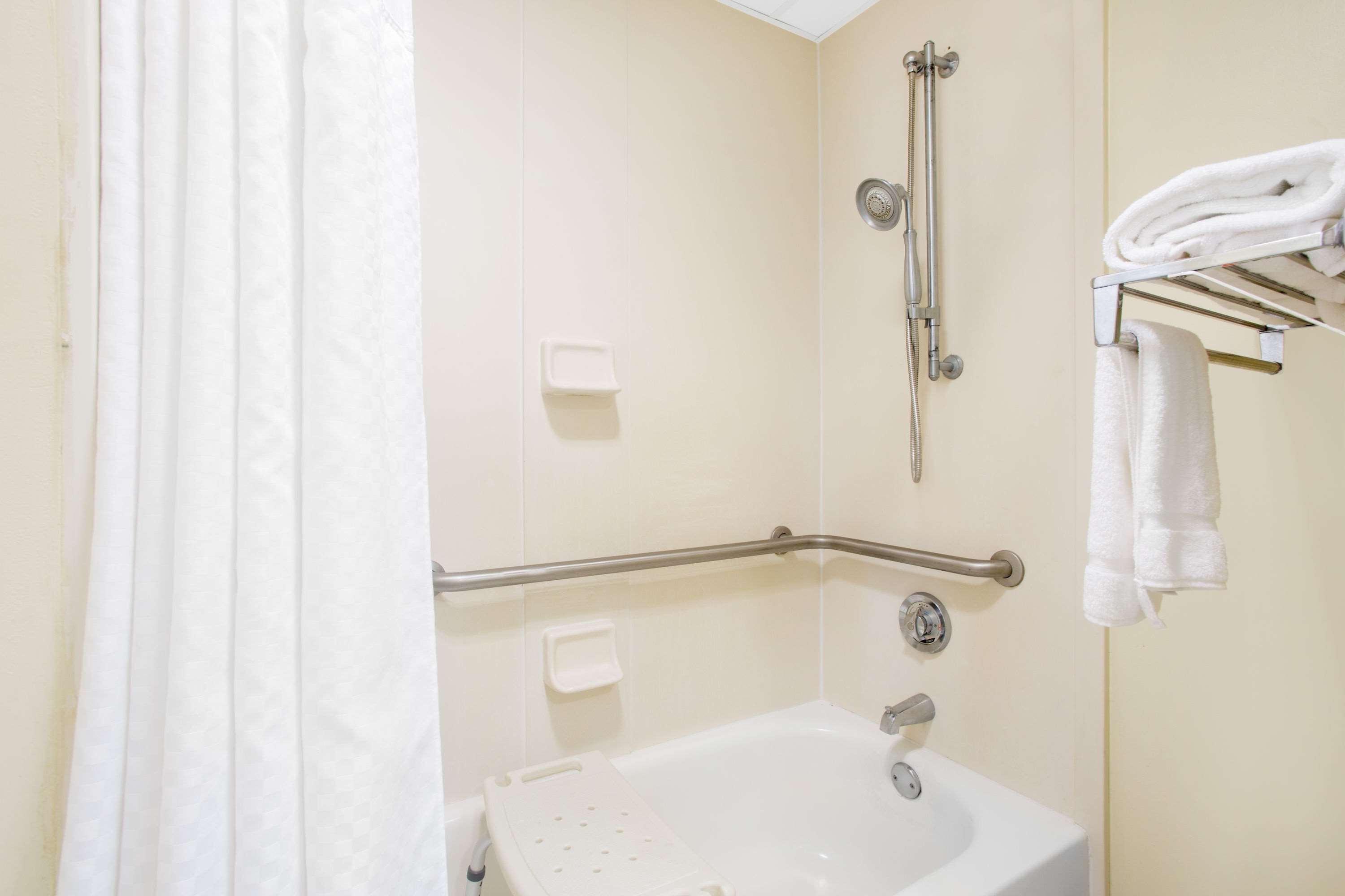 A bathroom with a bathtub, a shower, a grab bar, a towel rack, and a soap dispenser.