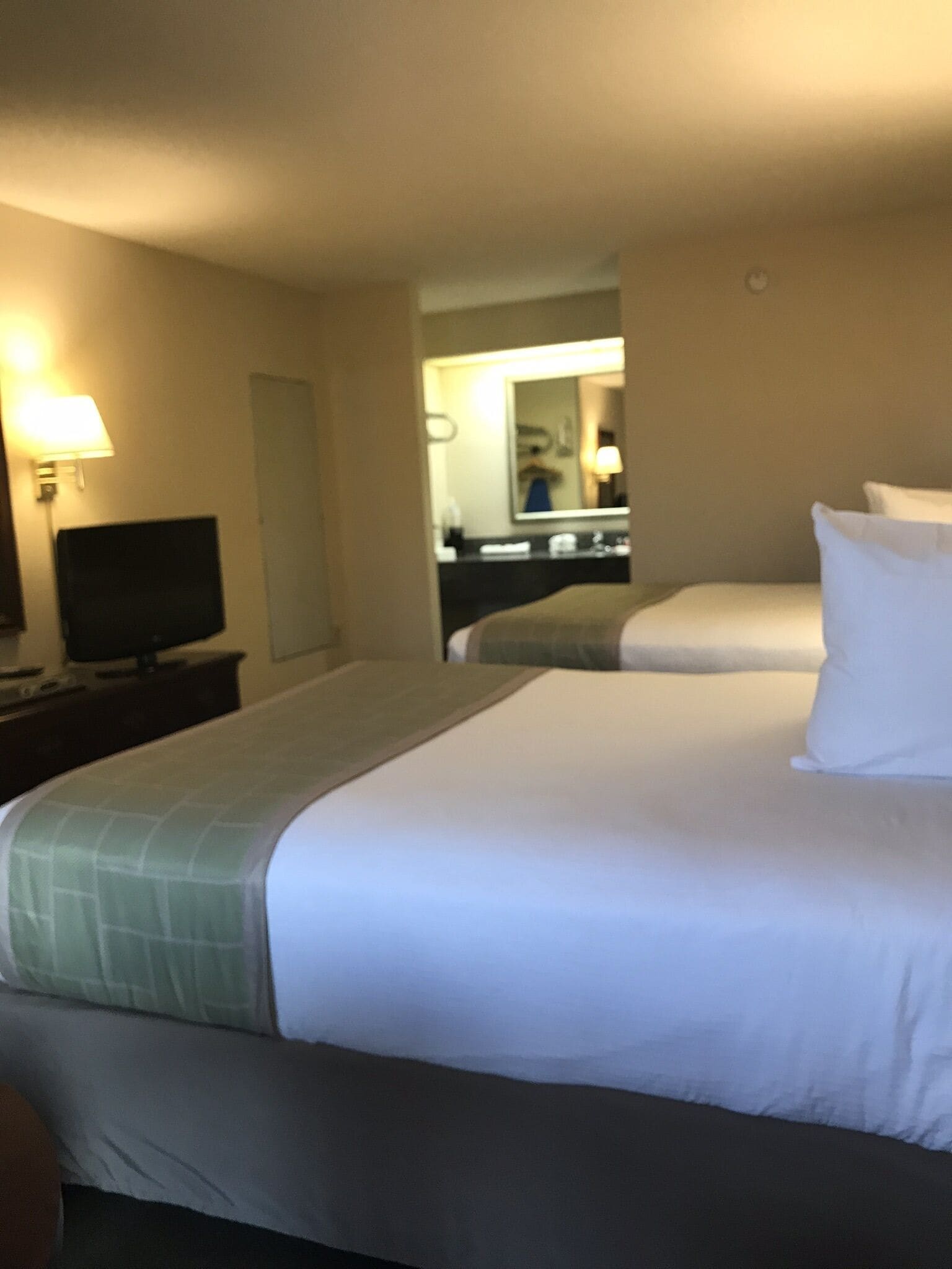 Habitación de hotel con dos camas, un televisor en una mesita de noche, un espejo y una lámpara.