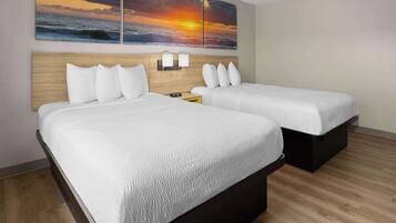 Habitación de hotel con dos camas, cabecera de madera, lámpara de pared y una pintura de atardecer.