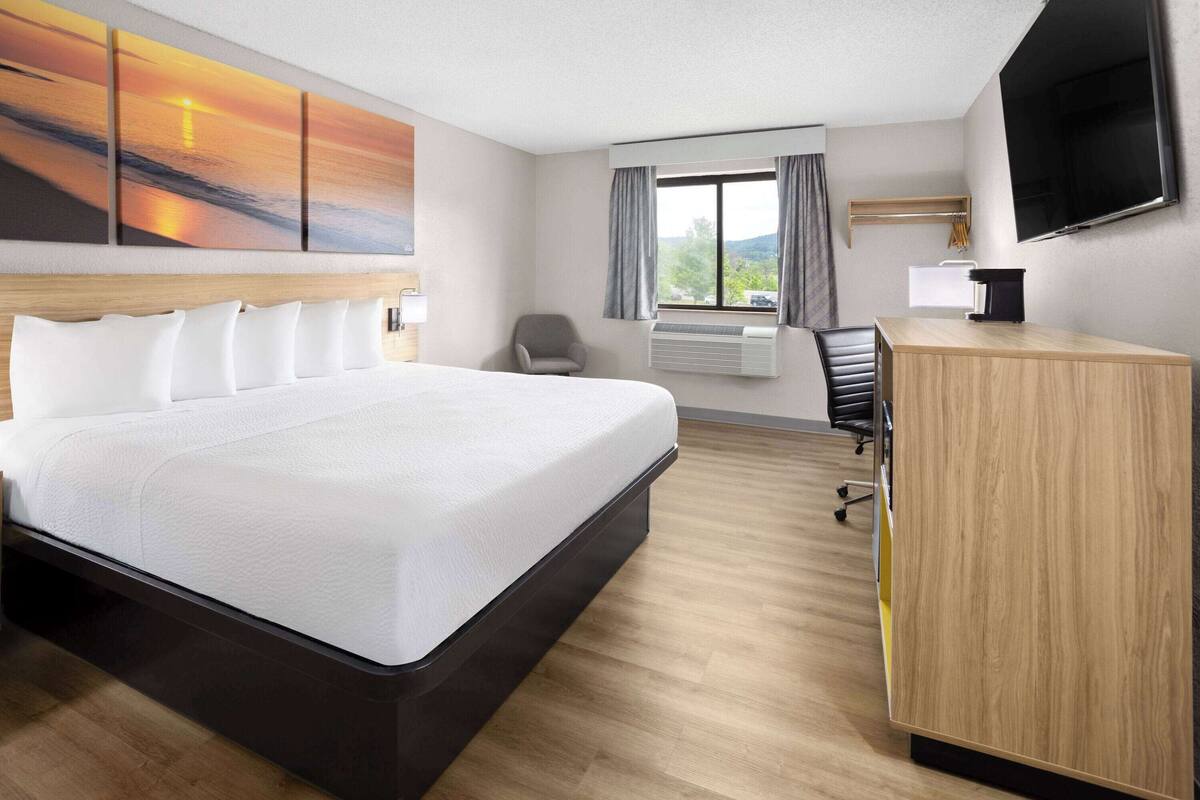 Une chambre d’hôtel avec un grand lit, un bureau, une chaise, une télévision et une fenêtre avec des rideaux.