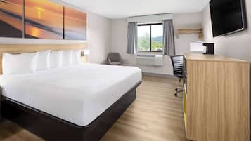 A hotel room with a large bed, a desk, a chair, a TV, and a window with curtains.