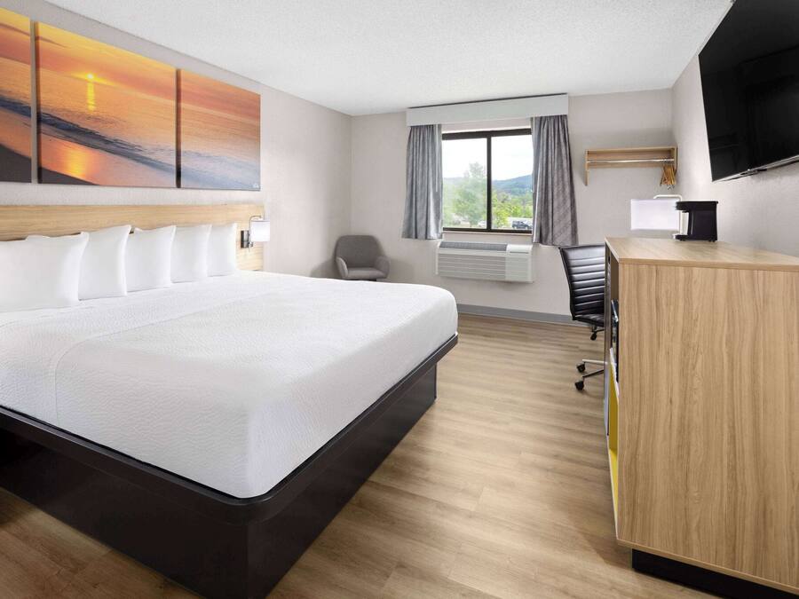A hotel room with a large bed, a desk, a chair, a TV, and a window with curtains.