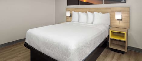 A hotel room with a large bed, wooden headboard, two bedside tables with lamps, and a wall-mounted painting of a sunset.