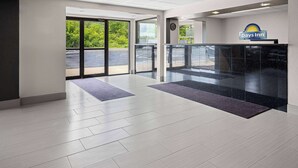 Een ontvangsthal van een Days Inn met een modern design, inclusief een receptiebalie, een klok en uitzicht op de parkeerplaats door grote glazen deuren.
