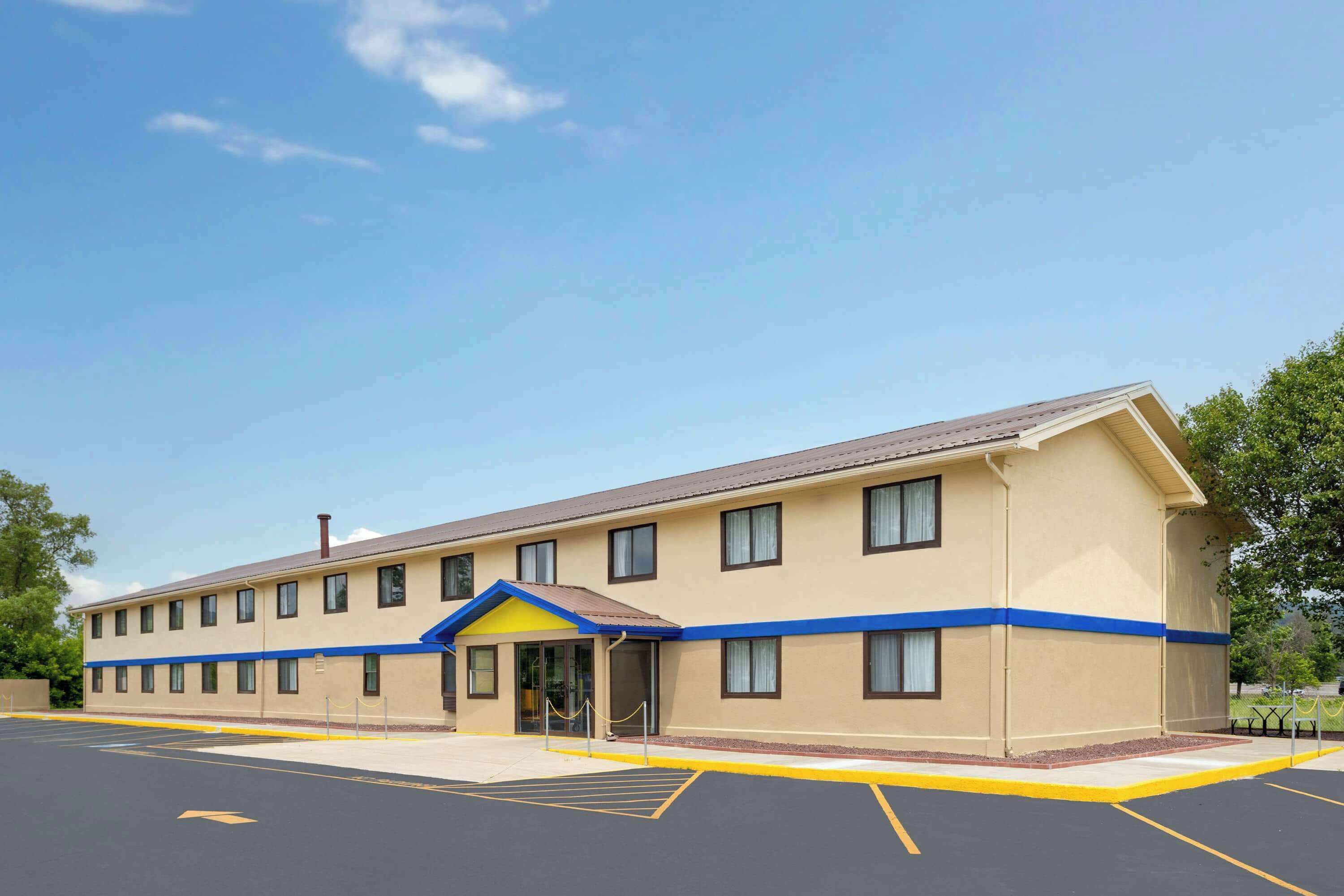 A two-story hotel with a flat roof, a yellow and blue facade, and a parking lot in front.