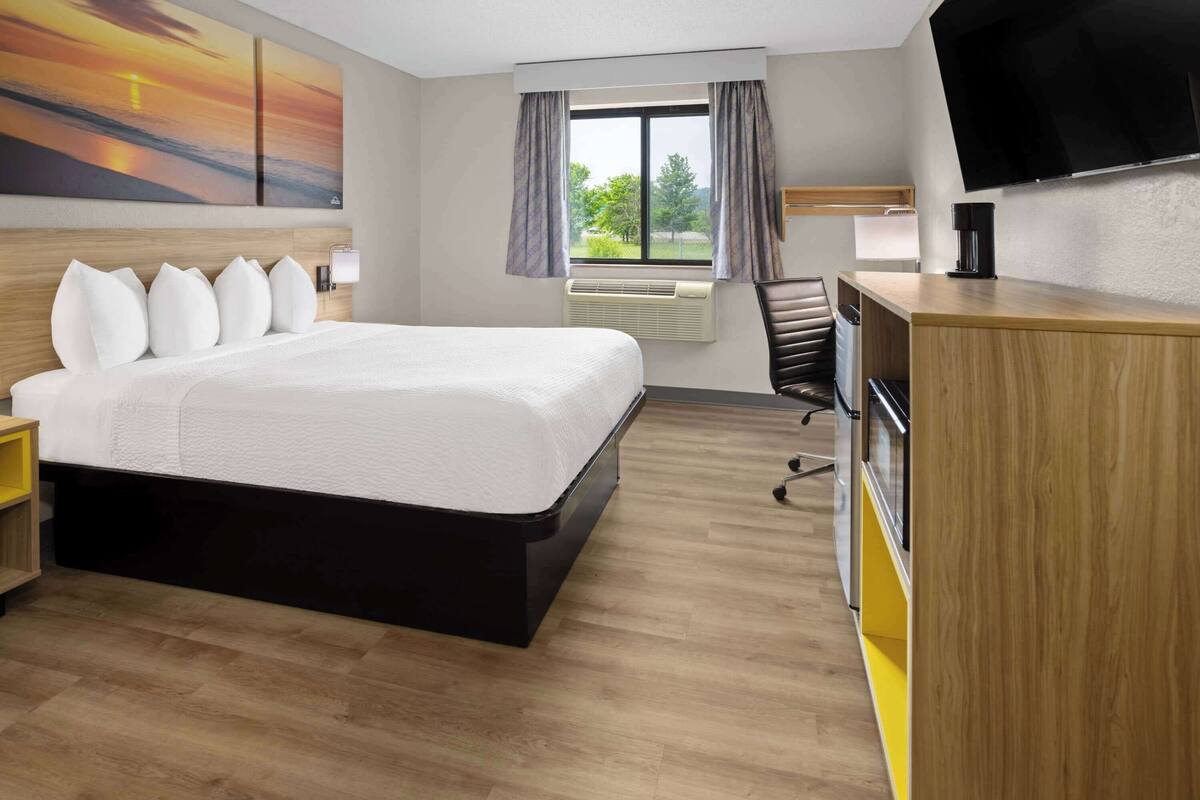 Une chambre d’hôtel avec un grand lit, un bureau, une chaise, un téléviseur à écran plat et une fenêtre avec des rideaux.