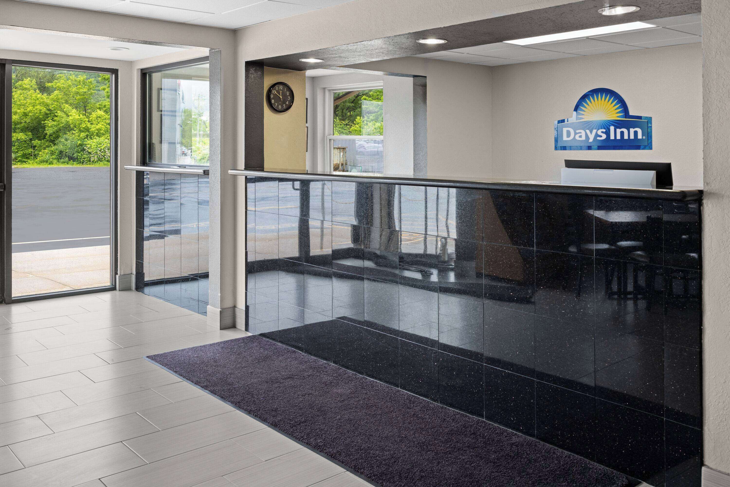 A Days Inn reception area with a glass partition, a clock, and a logo on the wall.