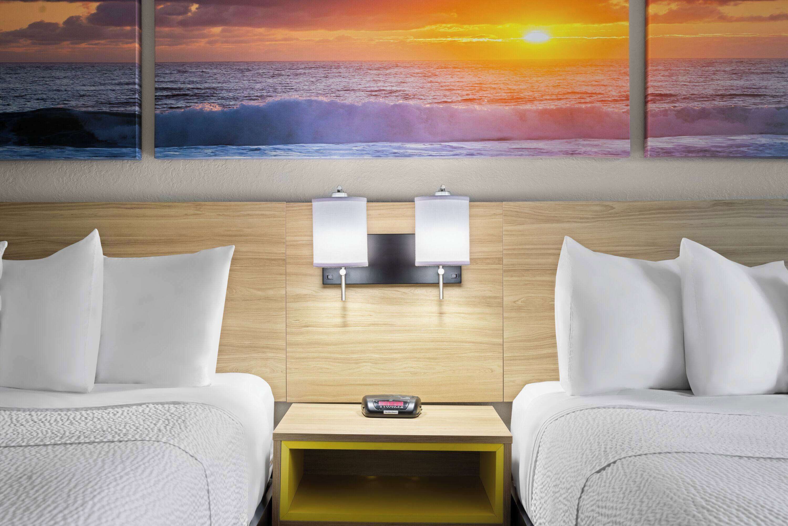 A hotel room with two beds, a nightstand, and a wall-mounted lamp.