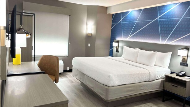 A hotel room with a bed, bedside table, desk, chair, and a wall-mounted TV.