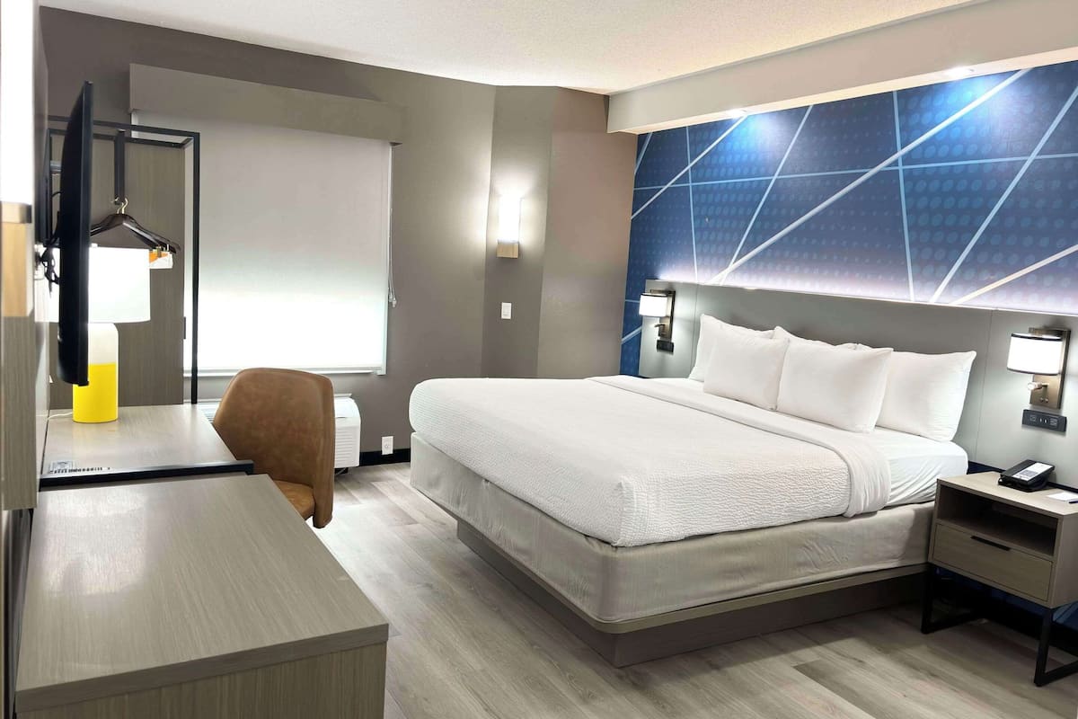 A hotel room with a bed, bedside table, desk, chair, and a wall-mounted TV.