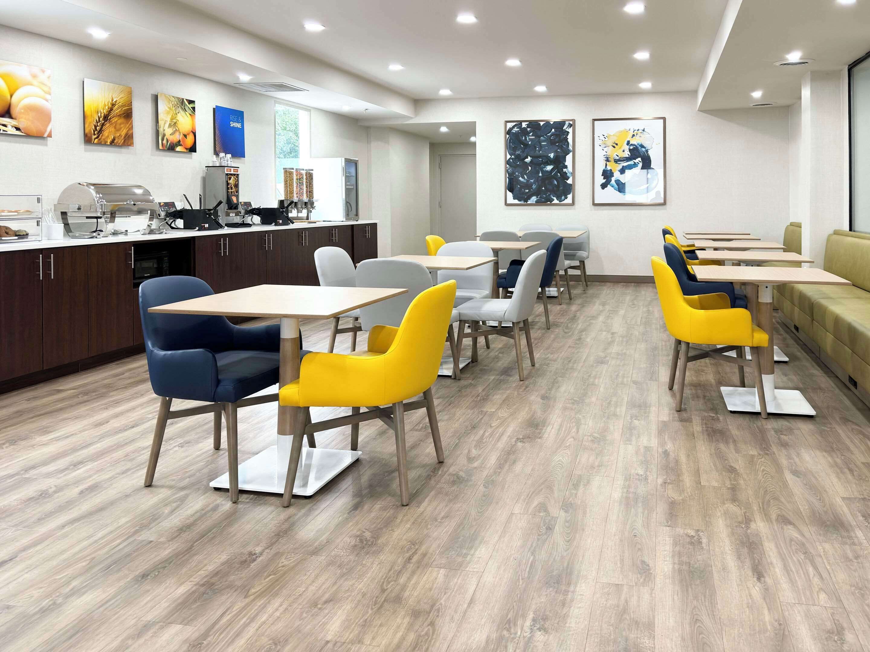 A modern dining area with wooden flooring, yellow and gray chairs, and a counter with kitchen appliances.