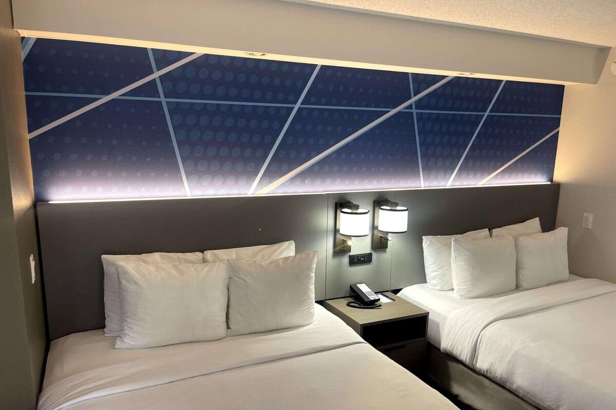 A hotel room with two beds, a nightstand with a phone and lamp, and a wall with a geometric pattern.