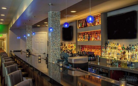 A bar area with a long counter, multiple seating options, and a variety of liquor bottles.