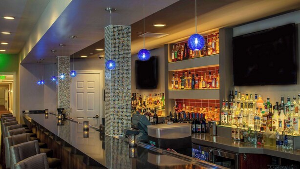 Zona de bar con una barra alargada, distintas opciones de asientos y una variedad de botellas de licores.