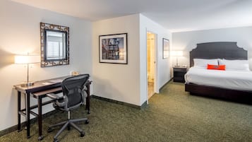 A hotel room with a bed, desk, chair, and two framed pictures on the wall.