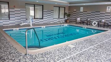 Ein Hallenbad mit gefliestem Boden und Wänden, einem Rettungsschwimmerstuhl und einem Schild mit der Aufschrift 'Nicht planschen'.