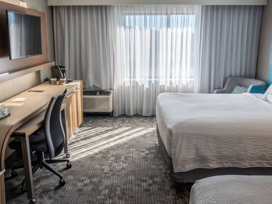 Habitación de hotel con una cama, un escritorio con silla, televisión en la pared y una ventana con cortinas.