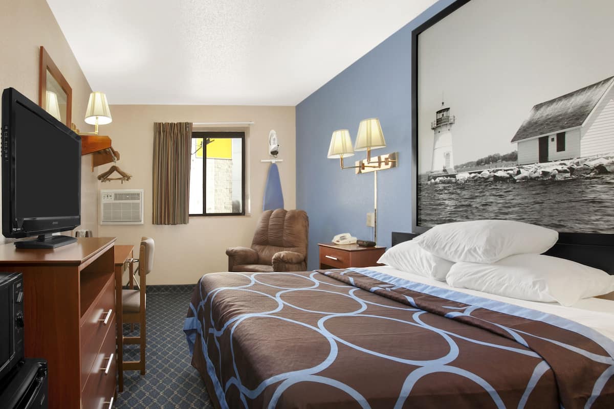 Ein Hotelzimmer mit Bett, Schreibtisch mit Fernseher, Stuhl, Nachttisch und Wandlampe.