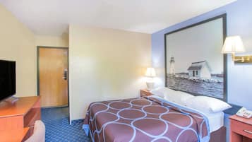 A hotel room with a bed, a desk with a TV, a nightstand with a lamp, and a large mirror reflecting a lighthouse and a house.