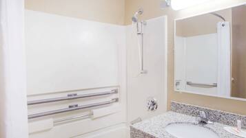 Un baño con lavamanos blanco, espejo y ducha con barras de apoyo.