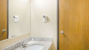 A bathroom with a granite countertop, a sink, a mirror, and two wall-mounted hair dryers.