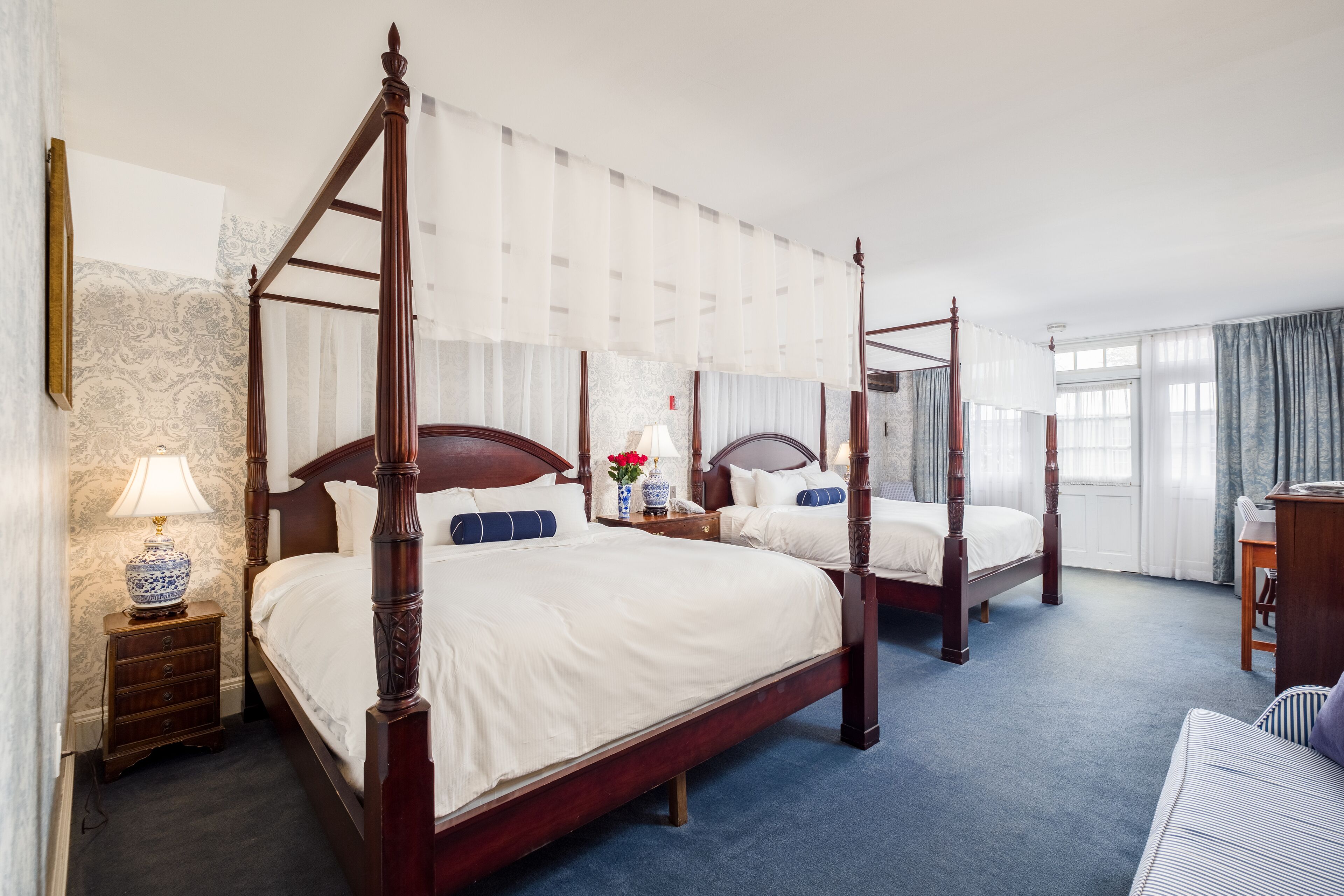 A four-poster bed with a wooden frame, a matching nightstand, a lamp, and a vase with flowers.