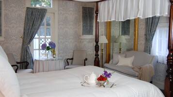 Una cama con dosel y cortinas, un área de descanso con un sofá, una mesita con un florero y una lámpara.