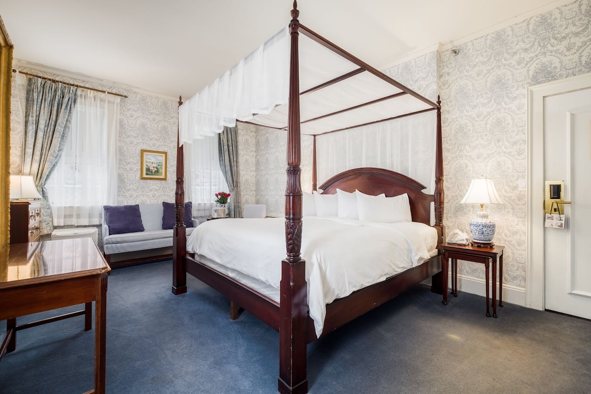 A four-poster bed in a hotel room with a sofa, a small table, and a lamp.