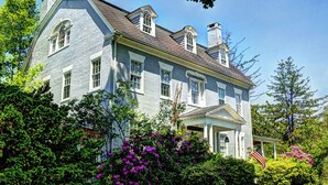 Une grande maison historique, dotée de nombreuses cheminées, d’un porche abrité et d’une végétation luxuriante.