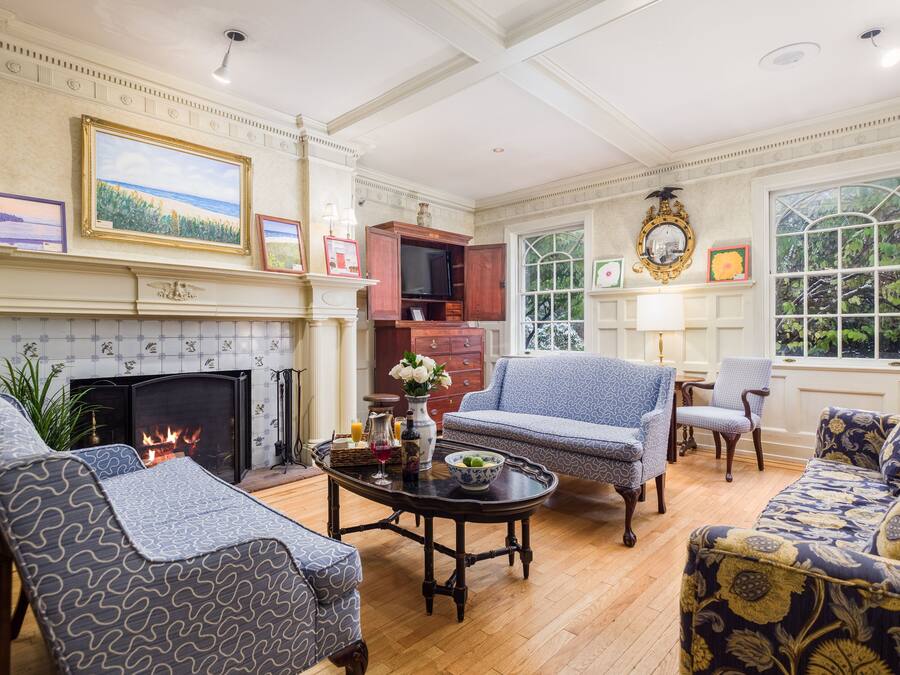 A traditional living room with a fireplace, patterned furniture, and a large window with a view of greenery.