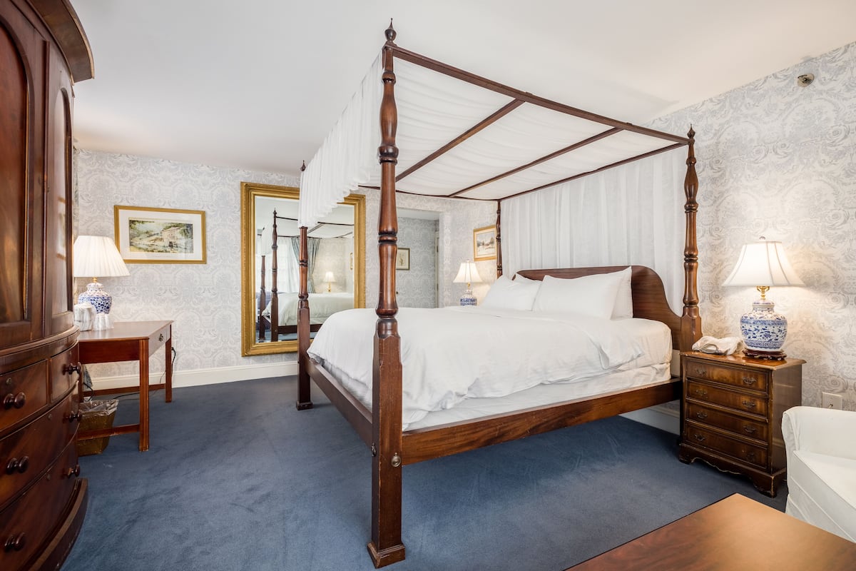 A four-poster bed with a wooden frame, a bedside table with a lamp, and a dresser with drawers.