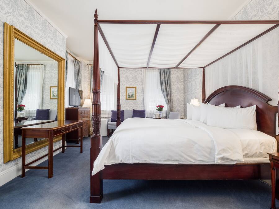 Una cama con dosel, un mesita de noche de madera, una mesita auxiliar y un espejo grande con marco dorado.