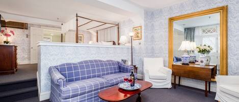 A room with a blue checkered sofa, a wooden coffee table with a vase and two glasses, a white armchair, and a large mirror.