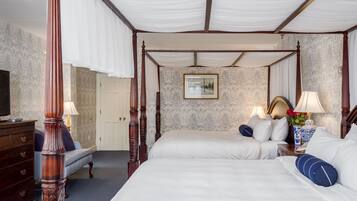 A four-poster bed with white linens, a wooden dresser, and a nightstand with a lamp.