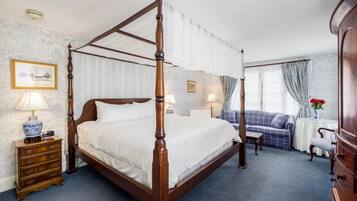 Een hemelbed met houten frame, een nachtkastje met lamp, een blauwe bank en een kleine tafel met bloevas.