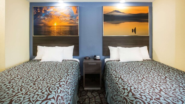 A hotel room with two beds, a nightstand, and two wall-mounted paintings of sunsets. - Days Inn by Wyndham Blue Springs (Blue Springs)