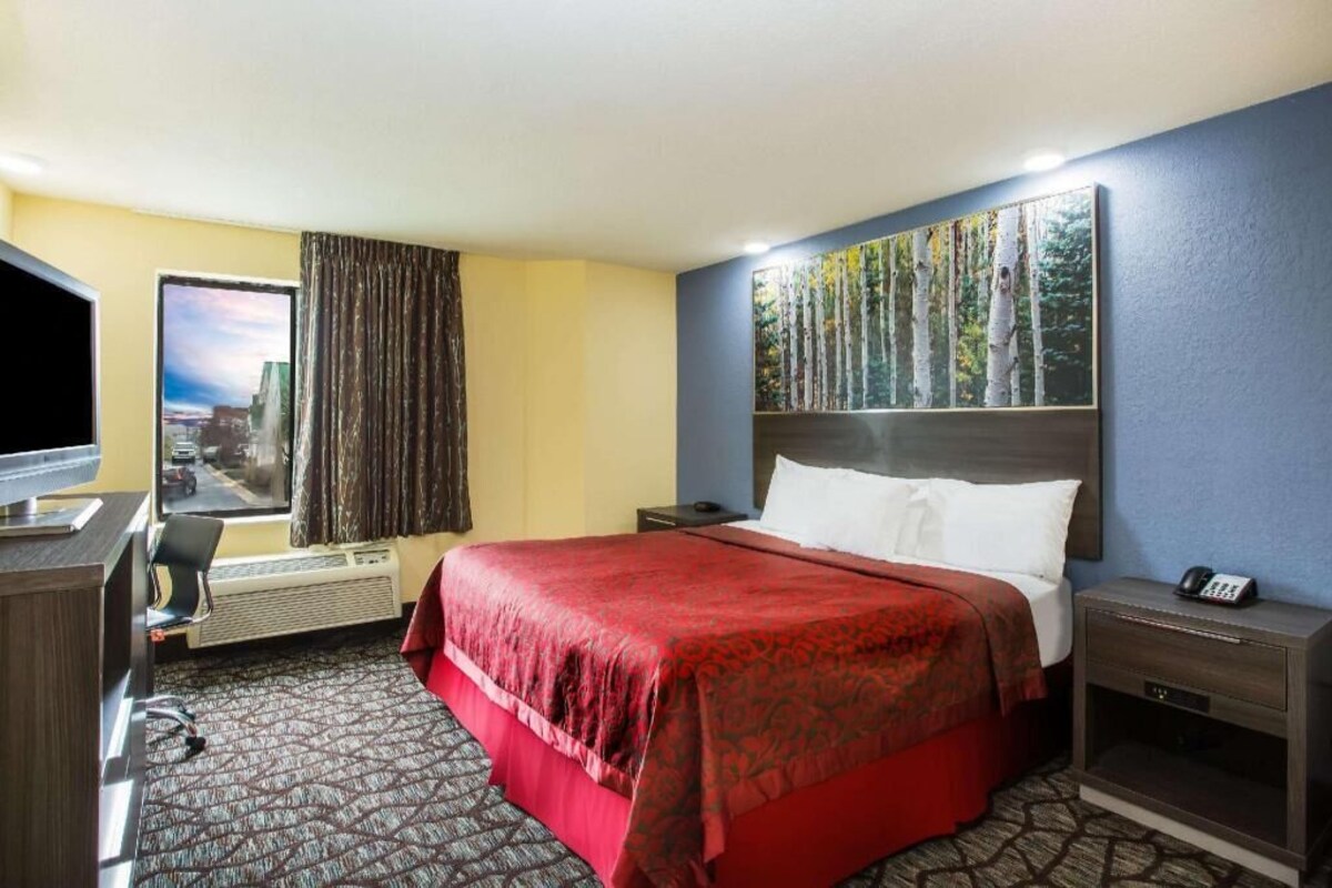 A hotel room with a bed, a desk with a chair, a TV, a phone, and a painting on the wall.