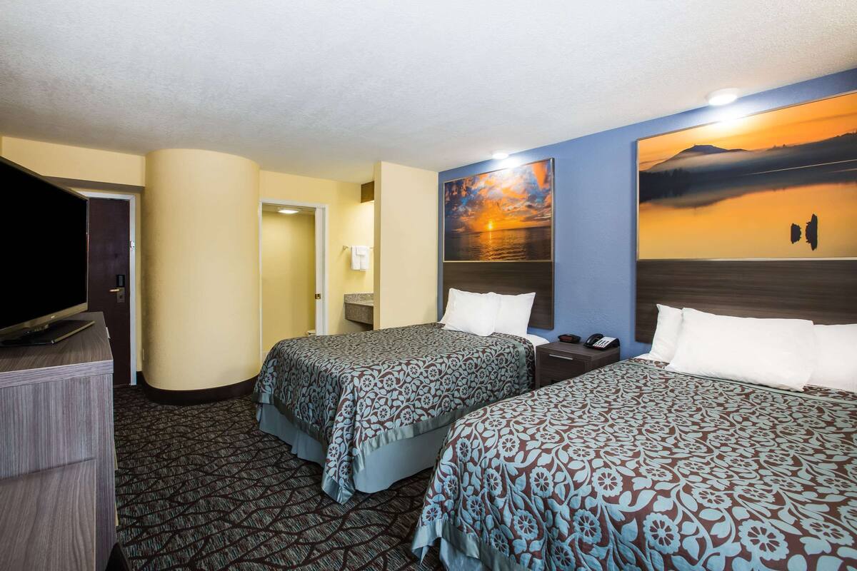 A hotel room with two beds, a TV, and a painting of a sunset.