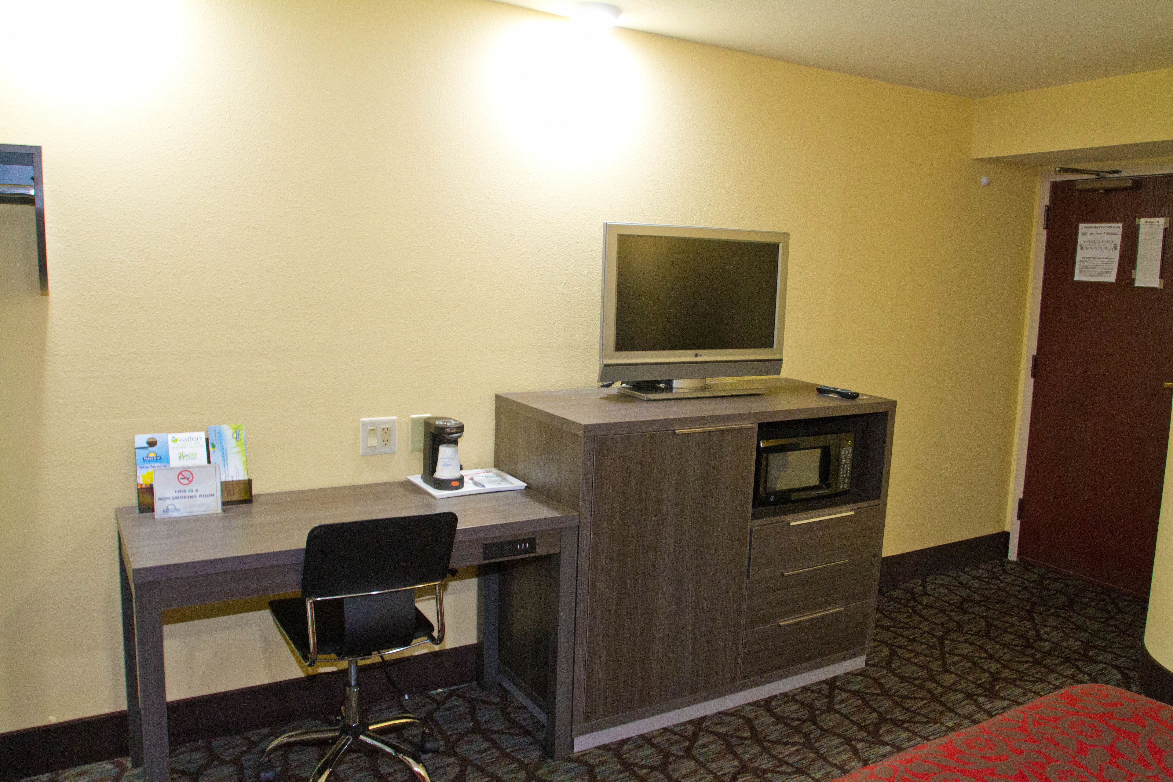 A hotel room with a desk, chair, microwave, and a television on a cabinet.