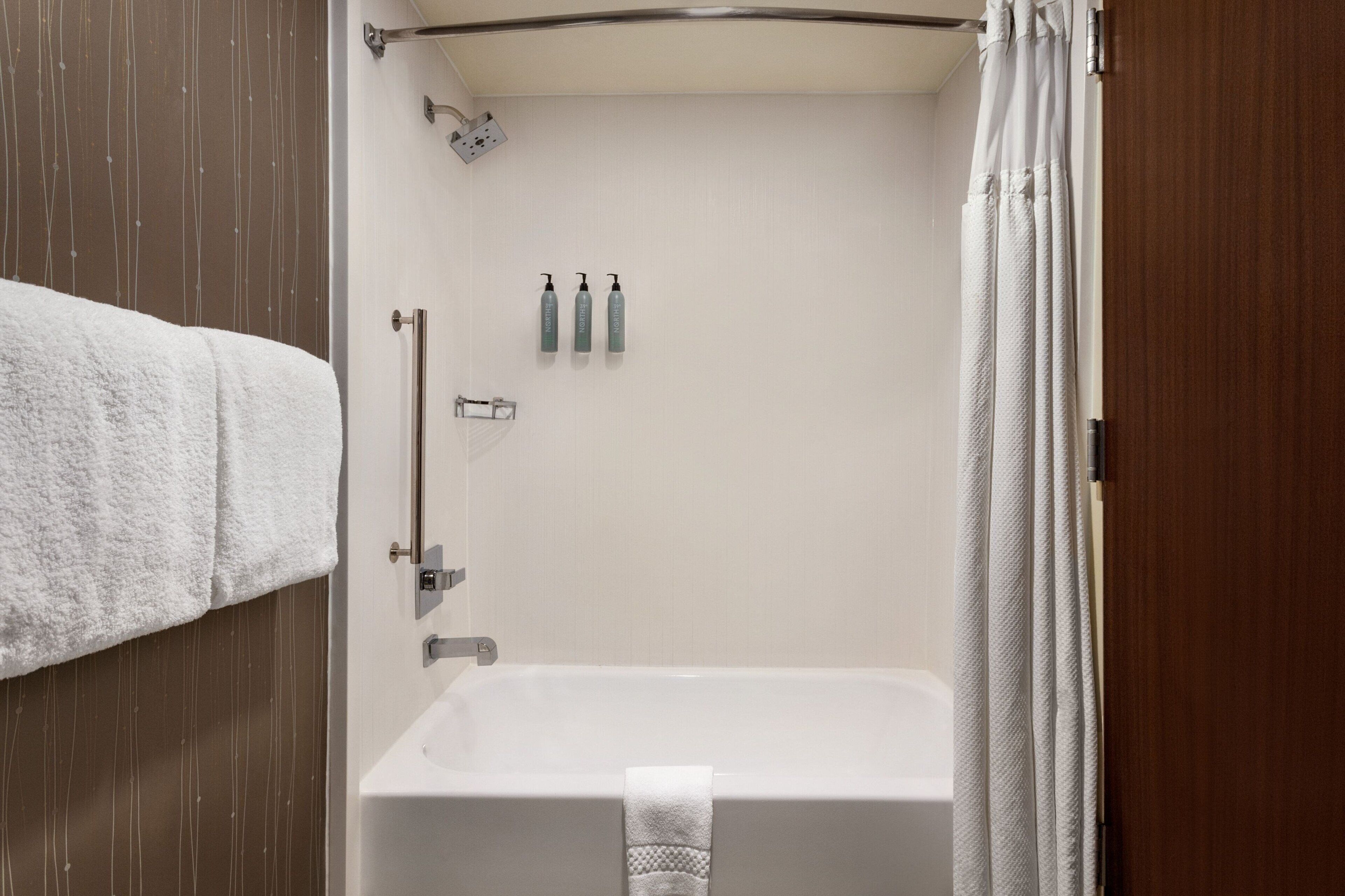 A bathroom with a bathtub, a towel rack, and two bottles of shampoo.