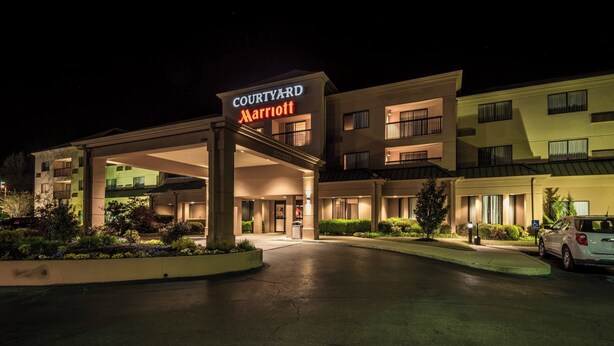 L’entrée d’un hôtel Courtyard Marriott, de nuit, avec une façade bien éclairée, un parking couvert et un jardin aménagé.
