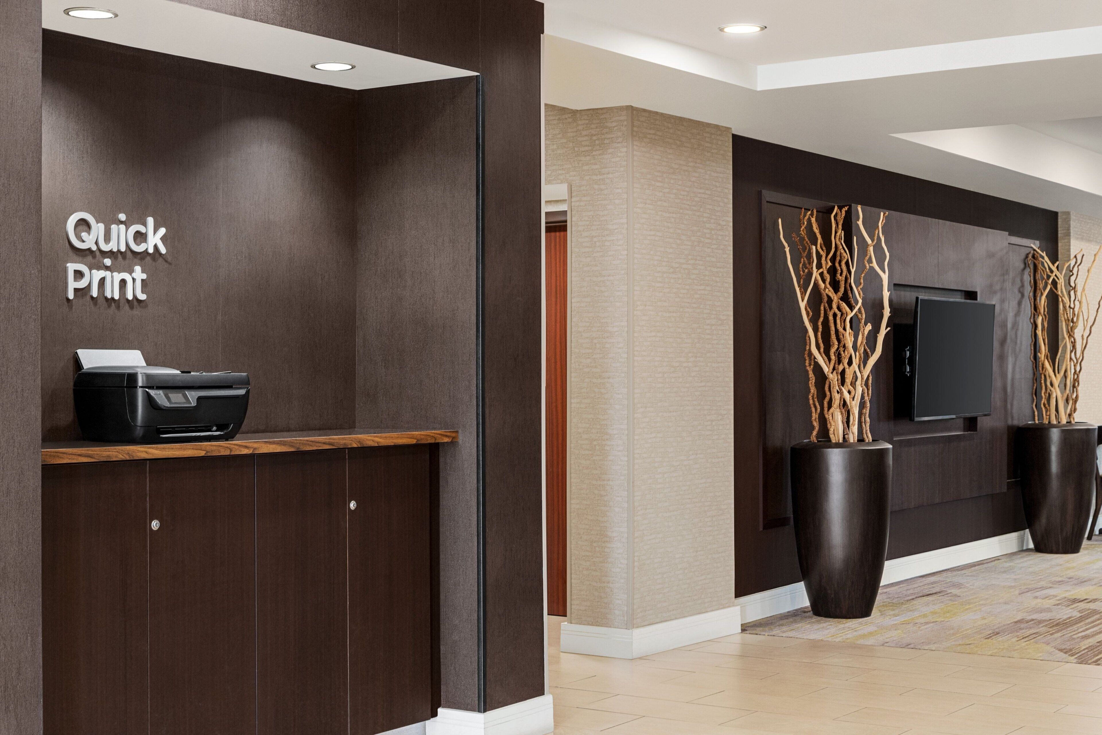 A reception area with a 'Quick Print' printer, a wooden counter, and two large potted plants.