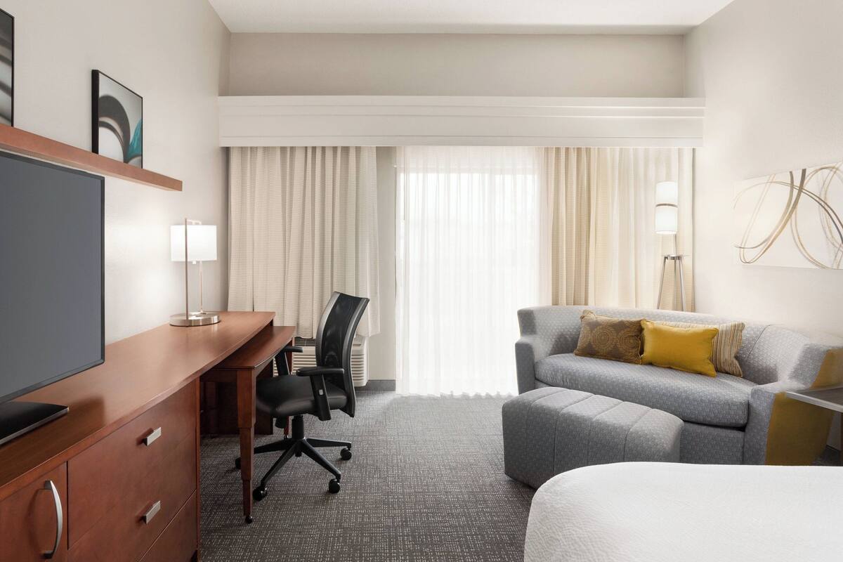 A hotel room with a bed, a desk with a chair, a sofa, and a television.