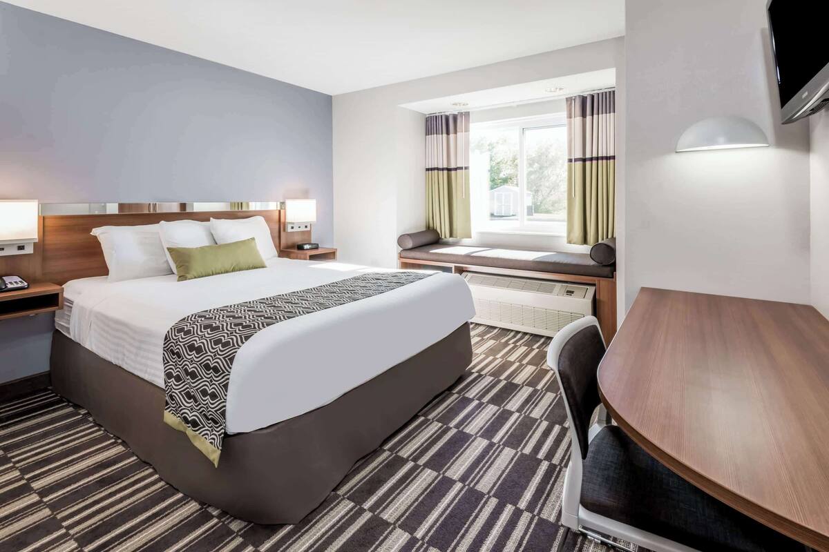 A hotel room with a large bed, bedside tables, a desk, a chair, and a window with curtains.