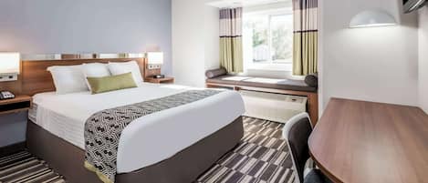 A hotel room with a large bed, bedside tables, a desk, a chair, and a window with curtains.