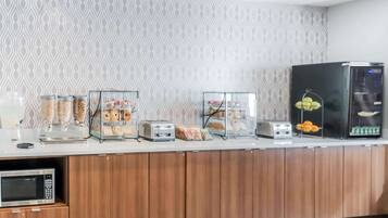Una barra de desayuno con diversos alimentos, un microondas y un refrigerador.