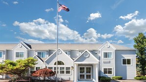 A two-story building with a gabled roof, a front porch, and a flagpole with an American flag. - Microtel Inn by Wyndham Victor/Rochester (Victor)