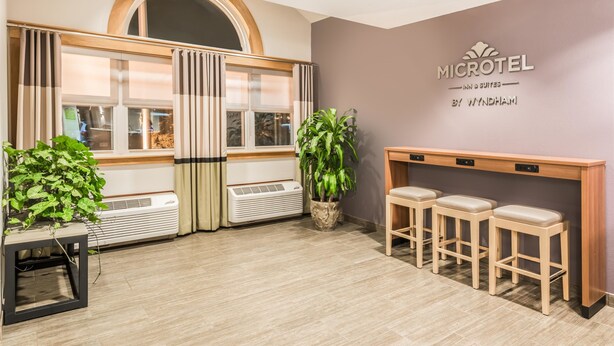 A hotel reception area with a modern design, featuring a reception desk, seating area, and a large window with curtains. - Microtel Inn by Wyndham Victor/Rochester (Victor)